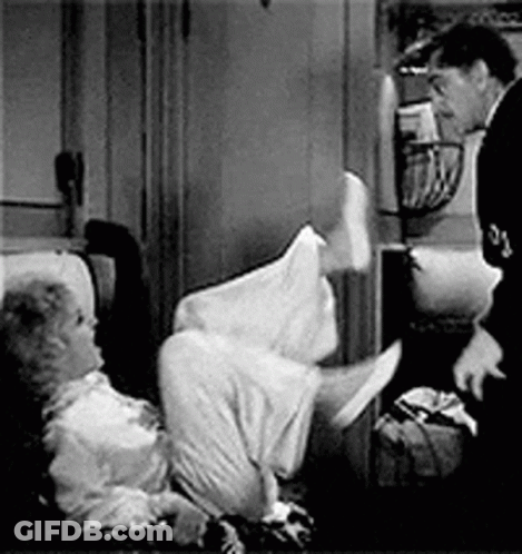 A Man Is Standing Next To A Woman Laying On A Couch . GIF