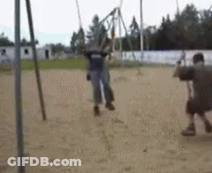 A Man Is Standing Next To A Woman On A Swing In A Playground . GIF