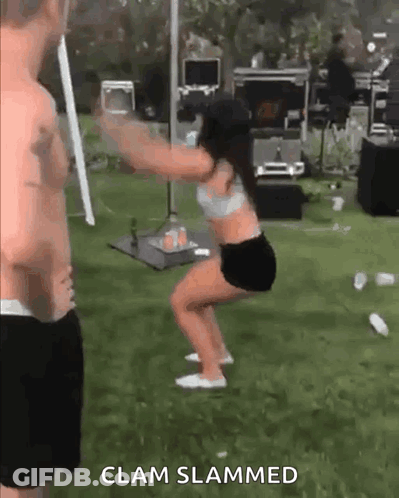 A Man Is Standing Next To A Woman Squatting In The Grass . GIF