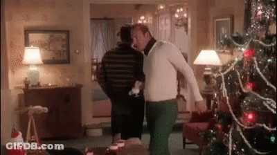 A Man Is Standing Next To Another Man In A Living Room With A Christmas Tree In The Background . GIF