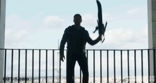 A Man Is Standing On A Balcony Holding A Large Sword In His Hand . GIF