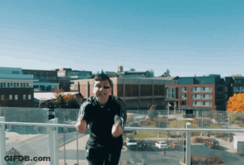 A Man Is Standing On A Balcony In Front Of A City GIF