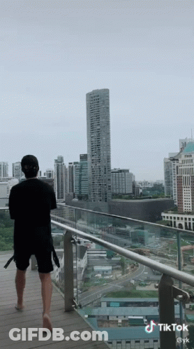 A Man Is Standing On A Balcony Looking At A City Skyline GIF
