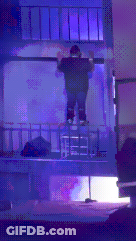 A Man Is Standing On A Balcony With A Blue Light Behind Him GIF