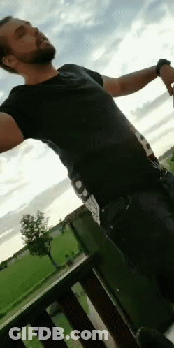 A Man Is Standing On A Balcony With His Arms Outstretched . GIF