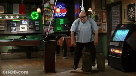 A Man Is Standing On A Barrel In A Bar With A Light Beer Sign Behind Him . GIF