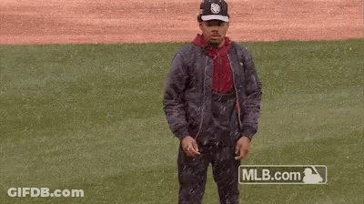 A Man Is Standing On A Baseball Field Wearing A Jacket And Hat . GIF