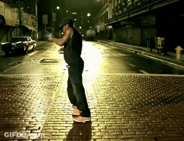 A Man Is Standing On A Brick Sidewalk At Night With A Fire Hydrant In The Background GIF