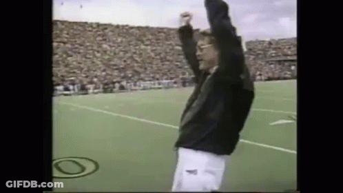 A Man Is Standing On A Field With His Arms In The Air . GIF