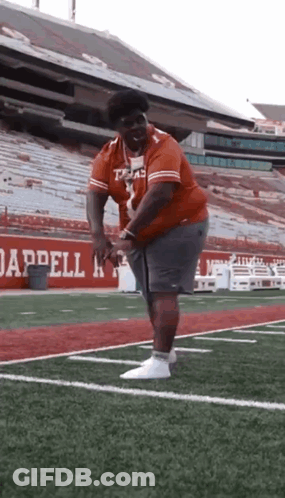 A Man Is Standing On A Football Field In Front Of A Stadium . GIF