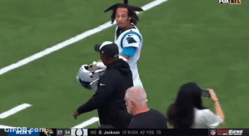 A Man Is Standing On A Football Field Talking To A Player . GIF