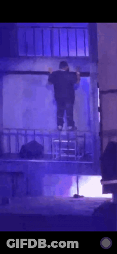 A Man Is Standing On A Ladder In A Dark Room With Blue Lights Behind Him . GIF