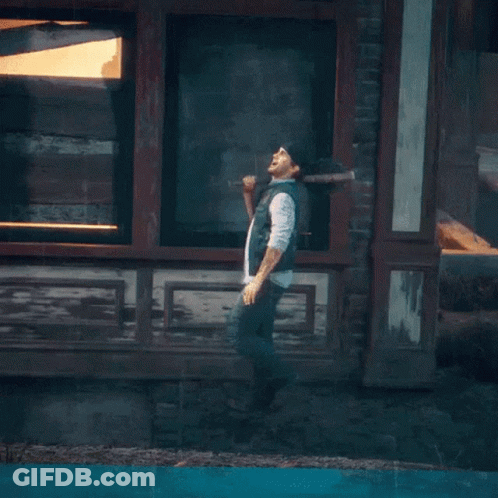 A Man Is Standing On A Lamp Post In Front Of A Brick Wall With Graffiti On It That Says Riot GIF