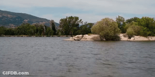 A Man Is Standing On A Rock In The Middle Of A Lake GIF