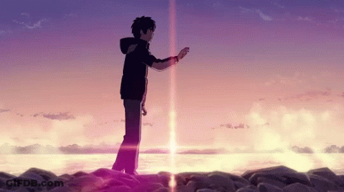 A Man Is Standing On A Rocky Beach Next To The Ocean At Sunset . GIF