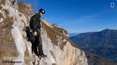 A Man Is Standing On A Rocky Cliff With The Words Running Wild Bear Grylls On The Bottom GIF