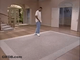 A Man Is Standing On A Rug In A Living Room With Stairs . GIF