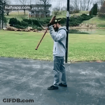 A Man Is Standing On A Sidewalk Holding A Cane And A Bat . GIF