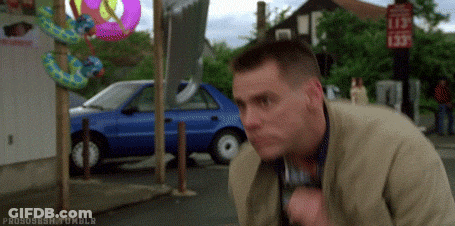 A Man Is Standing On A Sidewalk In Front Of A Blue Car And Talking On A Cell Phone . GIF