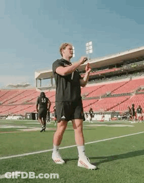 A Man Is Standing On A Soccer Field Holding A Frisbee . GIF