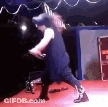 A Man Is Standing On A Stage Holding A Microphone And A Guitar . GIF