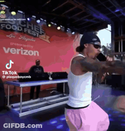 A Man Is Standing On A Stage Holding A Microphone In Front Of A Sign That Says Verizon . GIF