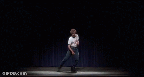 A Man Is Standing On A Stage In Front Of A Blue Curtain And Dancing . GIF