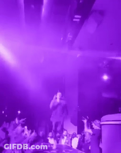 A Man Is Standing On A Stage In Front Of A Crowd In A Purple Room . GIF