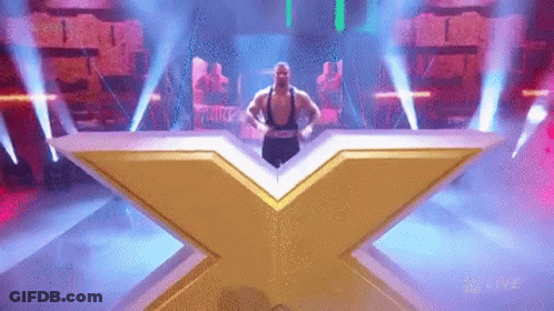 A Man Is Standing On A Stage In Front Of A Large X . GIF