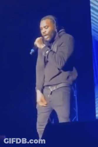 A Man Is Standing On A Stage Singing Into A Microphone . GIF