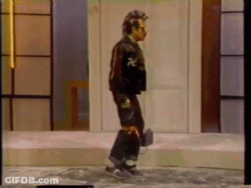A Man Is Standing On A Stage Wearing Headphones And A Skateboard . GIF