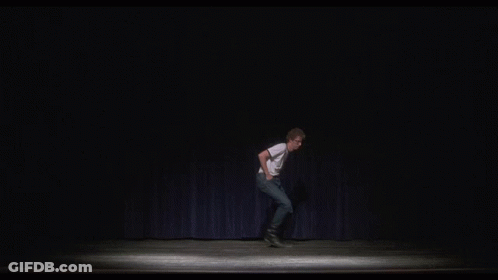 A Man Is Standing On A Stage With His Arms Outstretched And A Blue Curtain Behind Him . GIF