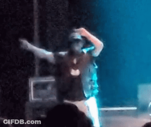 A Man Is Standing On A Stage With His Arms Outstretched And A Microphone In His Hand . GIF