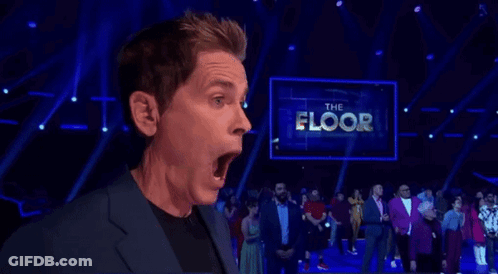 A Man Is Standing On A Stage With His Mouth Open In Front Of A Large Screen That Says The Floor . GIF