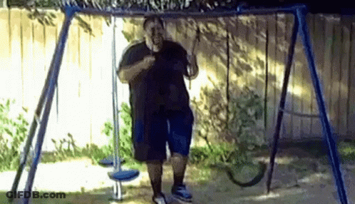 A Man Is Standing On A Swing In A Yard . GIF