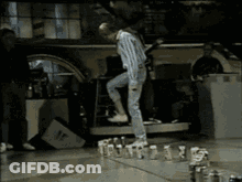 A Man Is Standing On A Table With A Bunch Of Bottles On It GIF