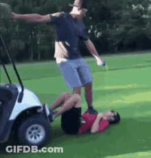 A Man Is Standing On Another Man 'S Back In A Golf Cart On A Golf Course . GIF
