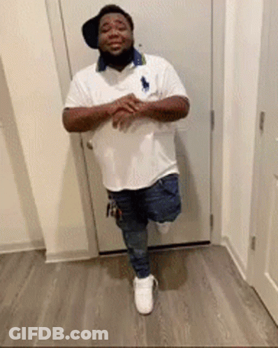 A Man Is Standing On One Leg In Front Of A Door Wearing A Hat And A White Shirt . GIF