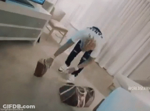 A Man Is Standing On The Floor In A Living Room Holding A Suitcase . GIF