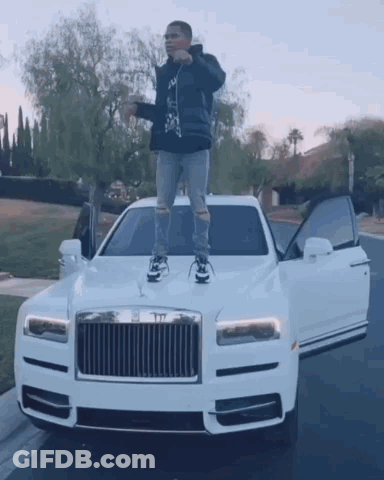 A Man Is Standing On The Hood Of A White Rolls Royce Car . GIF