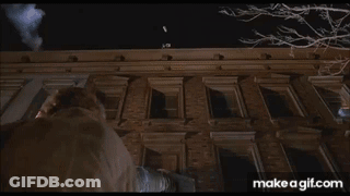 A Man Is Standing On The Roof Of A Tall Building At Night . GIF