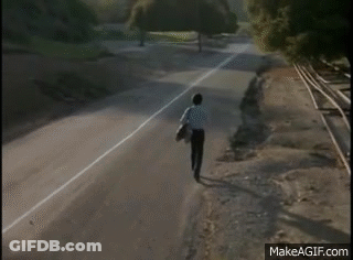 A Man Is Standing On The Side Of A Road Near Train Tracks . GIF