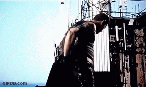 A Man Is Standing On Top Of A Building With A Gun . GIF