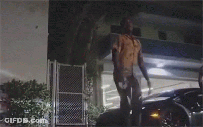 A Man Is Standing On Top Of A Car In Front Of A Building At Night . GIF
