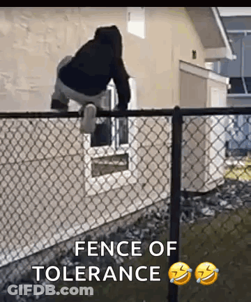 A Man Is Standing On Top Of A Chain Link Fence In Front Of A Window . GIF