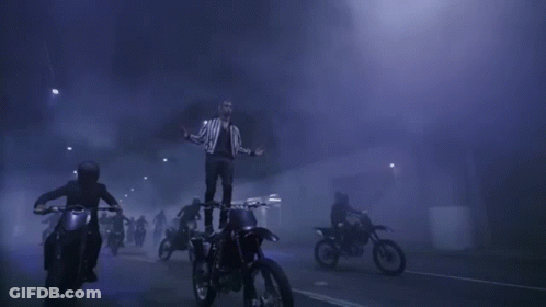 A Man Is Standing On Top Of A Dirt Bike In The Middle Of A Crowd Of People Riding Motorcycles . GIF