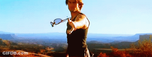 A Man Is Standing On Top Of A Mountain Holding A Pair Of Sunglasses In His Hand . GIF