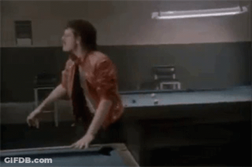 A Man Is Standing On Top Of A Pool Table In A Pool Hall . GIF