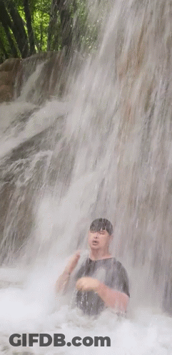A Man Is Standing Under A Waterfall With His Head In The Water GIF