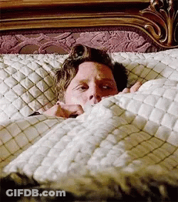 A Man Is Sticking His Head Out Of A Bed . GIF